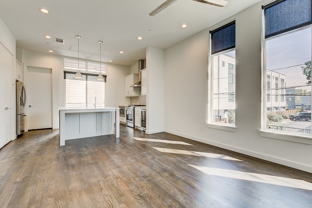 an empty living room with a kitchen and large windows