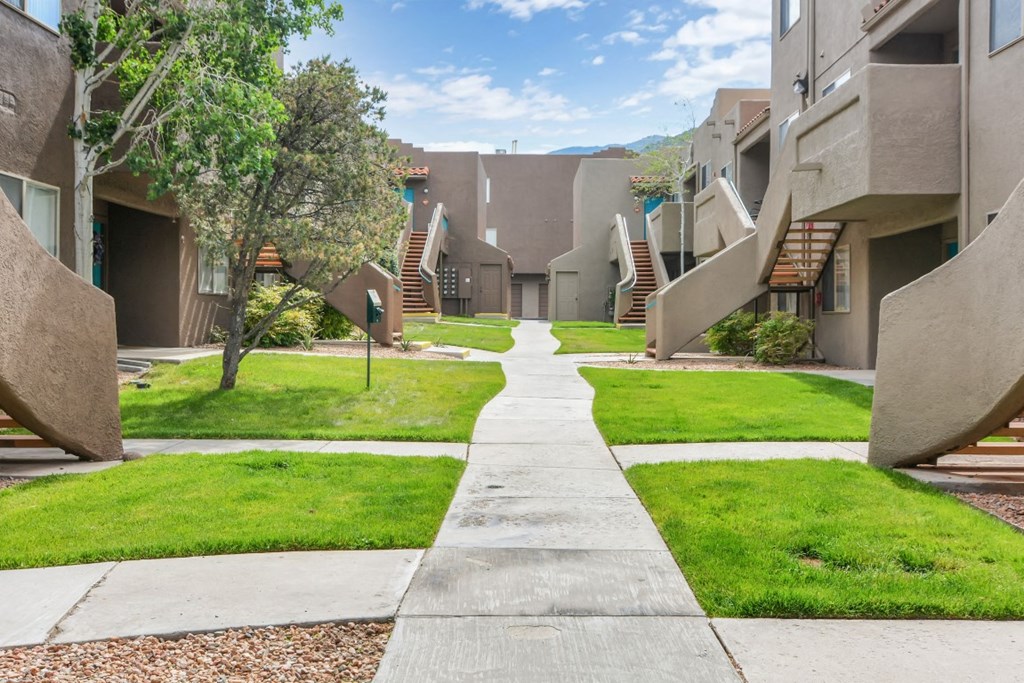 a pathway between two buildings with stairs and grass and trees