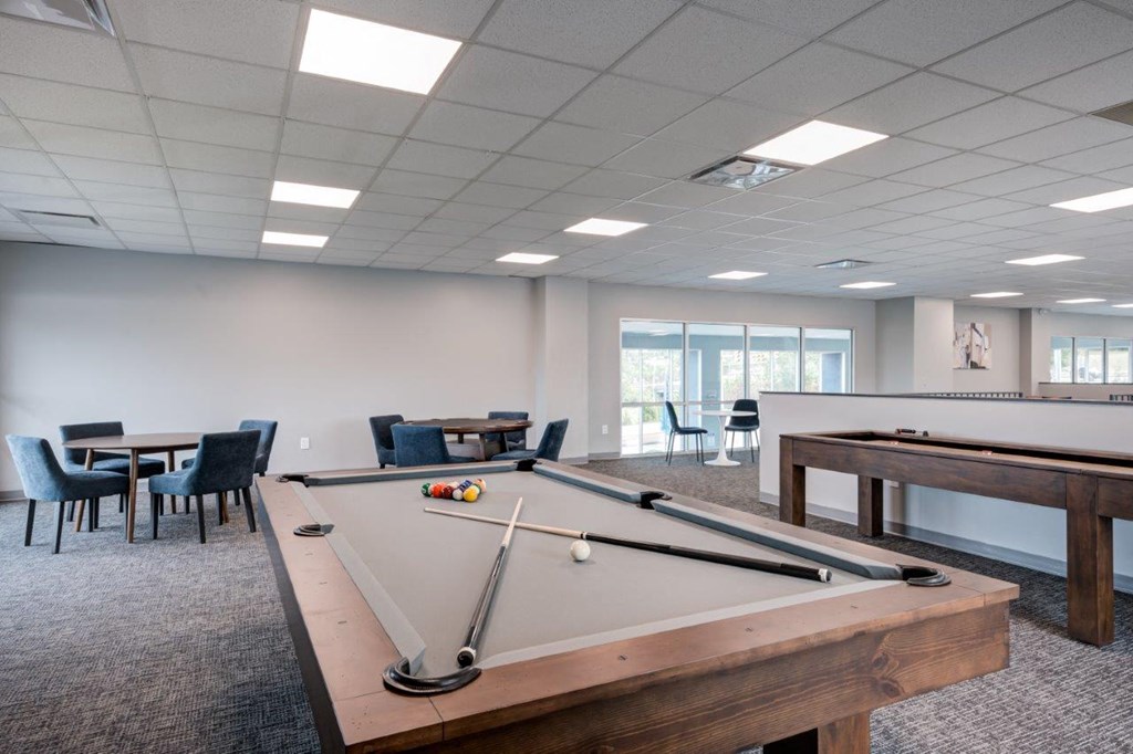 A pool table in a room with a carpeted floor and a dining table with chairs.