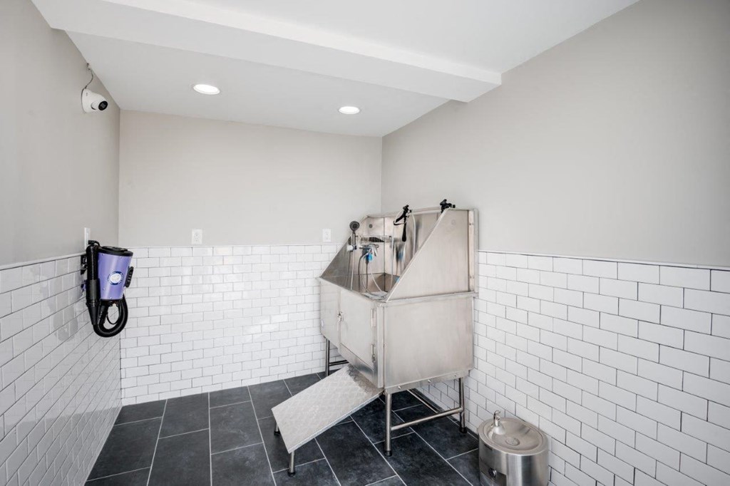 A white tiled bathroom with a shower stall and a trash can.