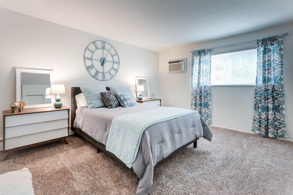A bedroom with a large bed, a clock on the wall, and a window with curtains.