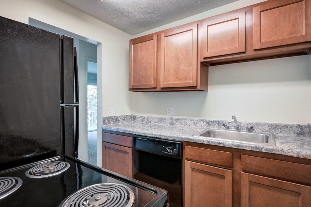 A kitchen with a black refrigerator and brown cabinets.
