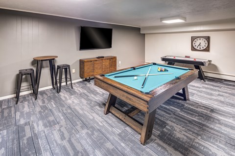 A room with a pool table, a TV, a clock, and a bar stool.