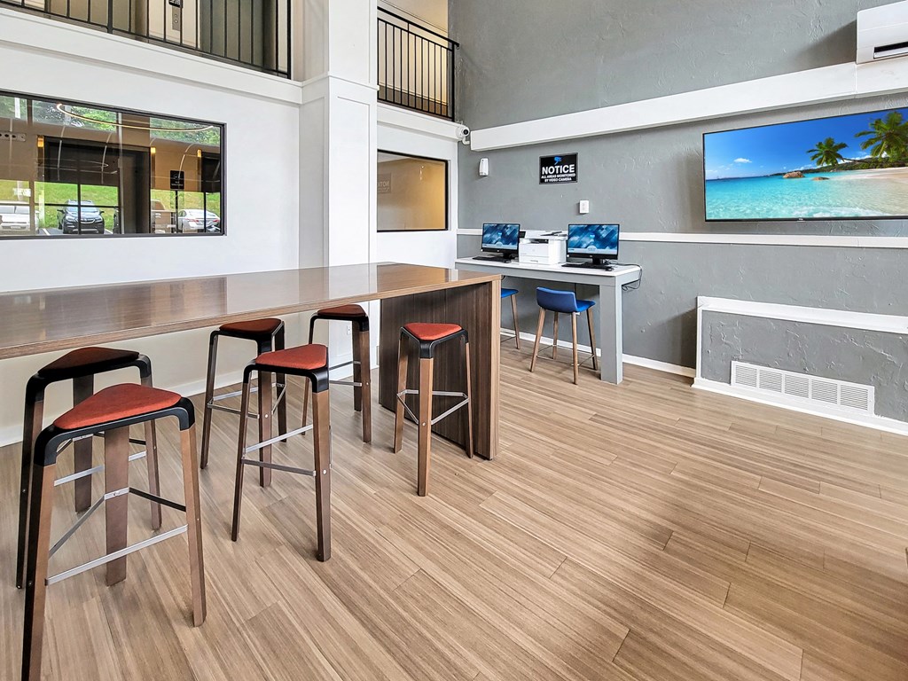 a common area with stools and a bar with computers and a television
