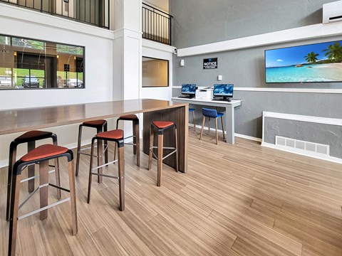 a common area with stools and a bar with computers and a television