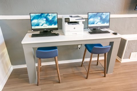 a white desk with two computers and two blue chairs