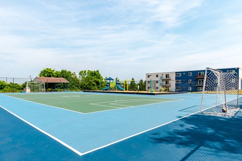 two tennis courts with buildings and trees in the background on a sunny day