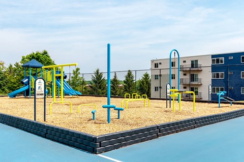 a playground with yellow and blue playground equipment in front of an apartment building