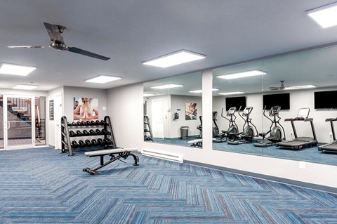 a spacious fitness room with cardio machines and mirrors