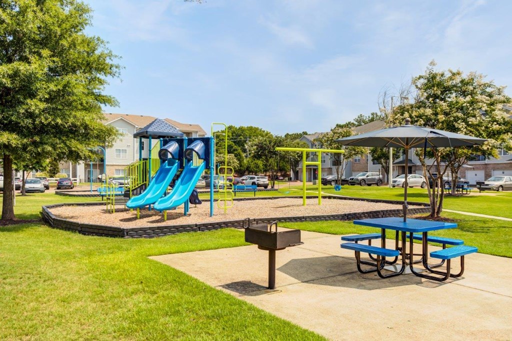 a playground with a blue slide and picnic table in a park