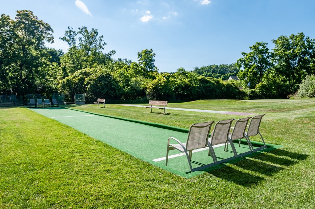 a park with benches on a green lawn and a tennis court