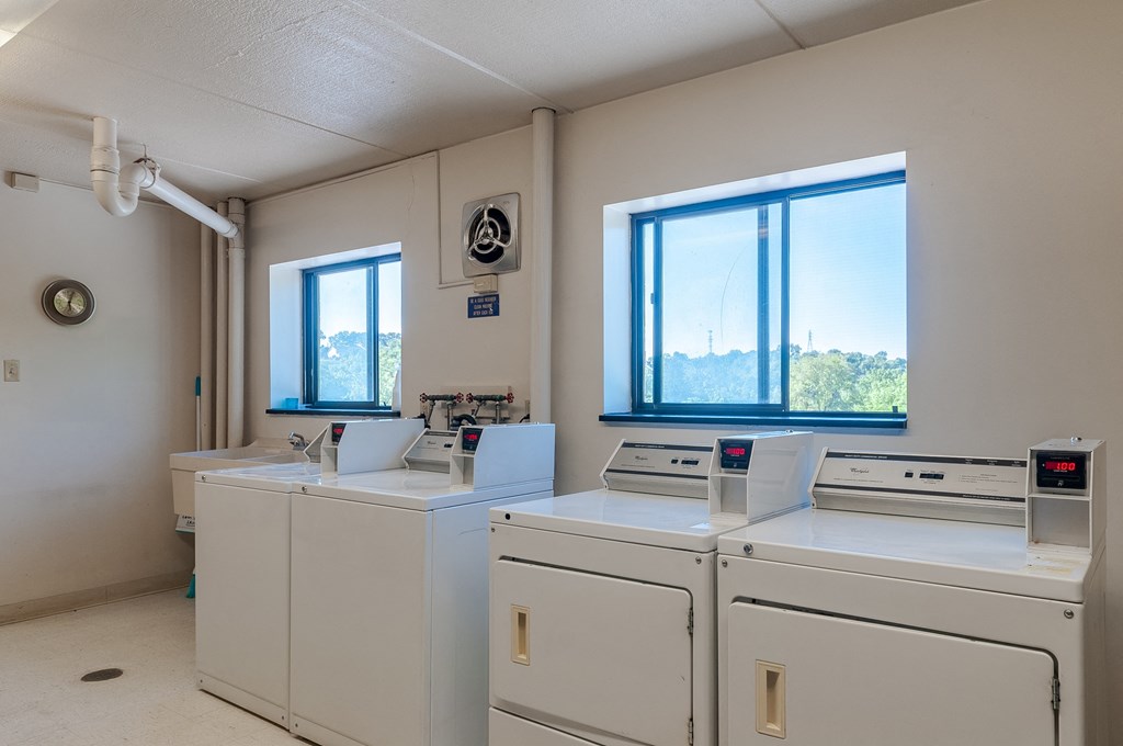 a laundry room with four washing machines and two windows