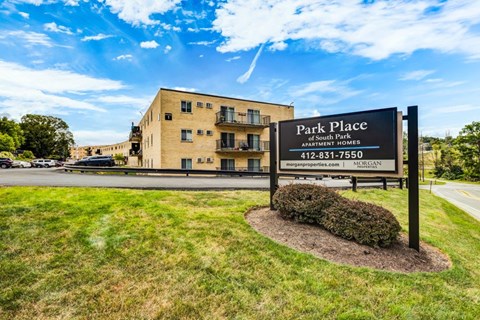 A sign for Park Place Apartment Homes stands in front of a tan building.