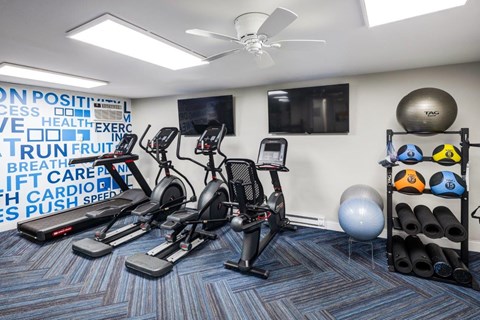 A gym room with exercise equipment and a wall of motivational words.