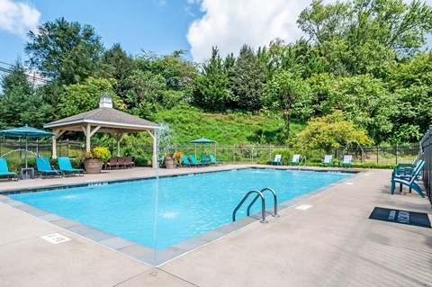 a swimming pool with chairs and a gazebo and trees