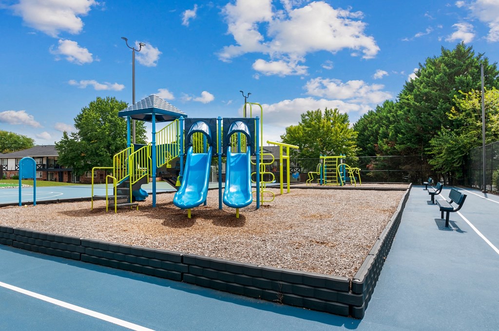 a playground with a blue and yellow swing set in a park