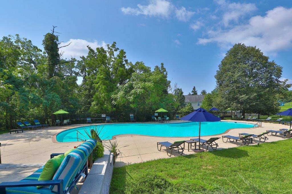 a swimming pool with tables and umbrellas in a park