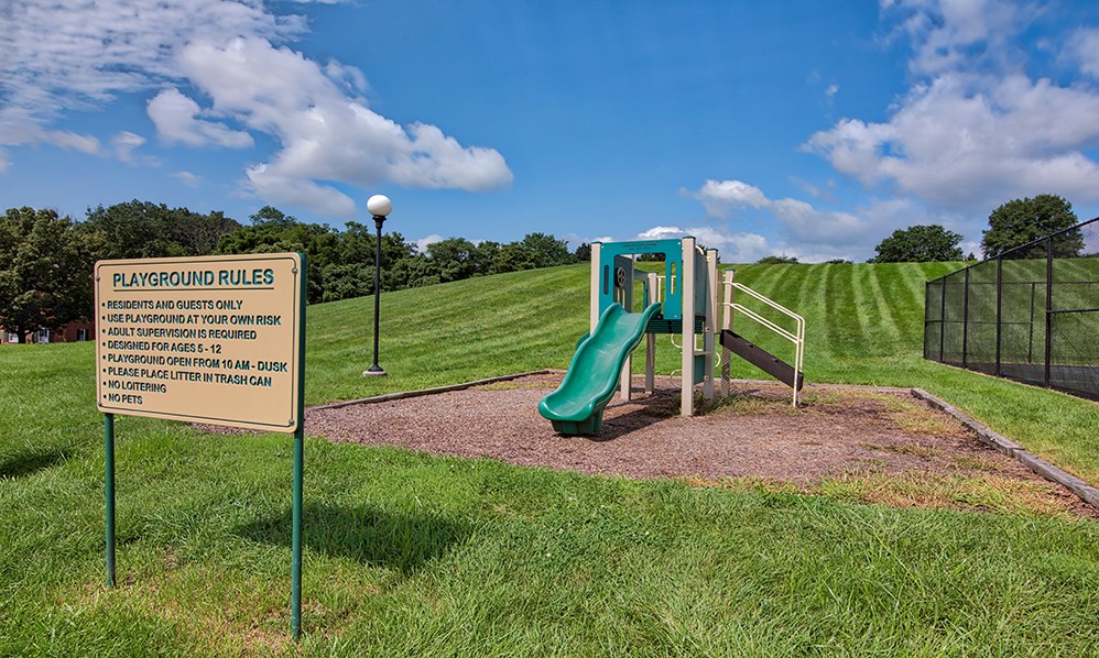 a playground with a green slide and a sign in the grass