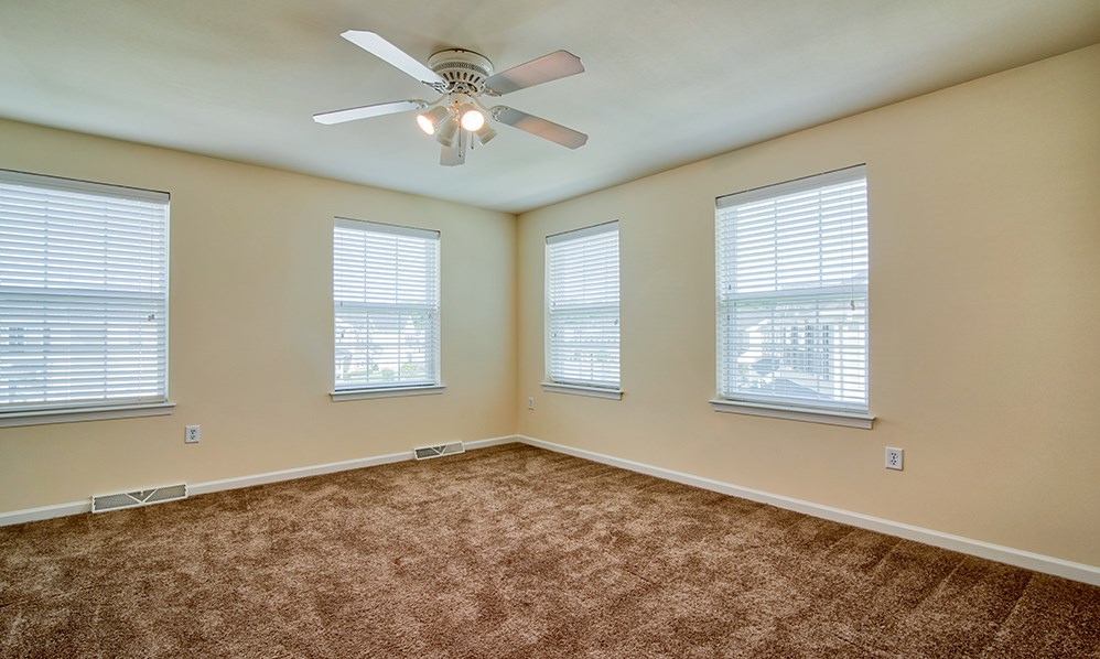 an empty living room with a ceiling fan and three windows