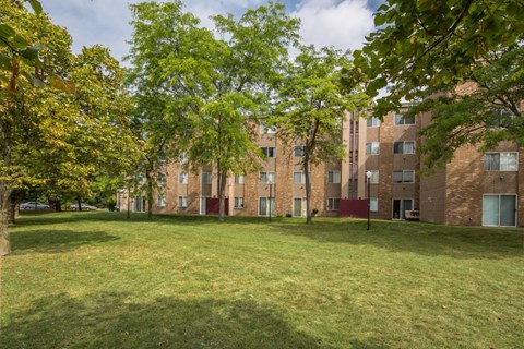 A grassy area in front of a brick building with trees on the left.