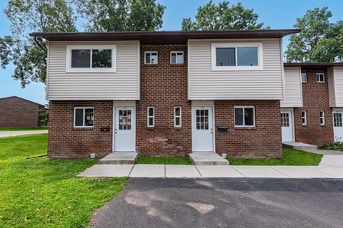 a white and brick house with white doors and a sidewalk