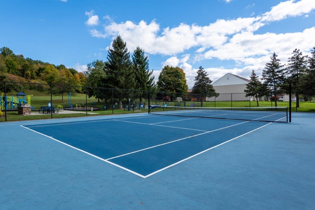 a tennis court at a park with trees and a building in the background
