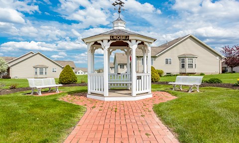 a gazebo with two benches and a house in the background