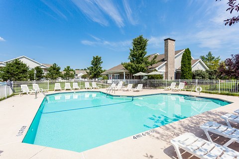 A large swimming pool surrounded by lawn chairs and trees.