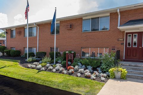 the front of a brick building with two flags and a flower garden