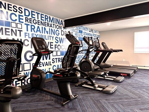 A gym with a row of stationary bikes in front of a wall with fitness related words.