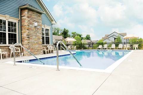A pool with a stone pillar and a house in the background.