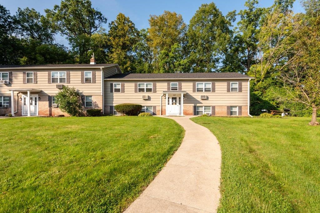 a walkway leading to a house with a lawn and trees