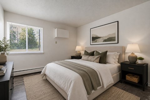 A bedroom with a large bed, a nightstand with a lamp, and a framed picture on the wall.