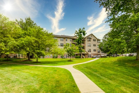 a sidewalk leading to an apartment building with green grass and trees