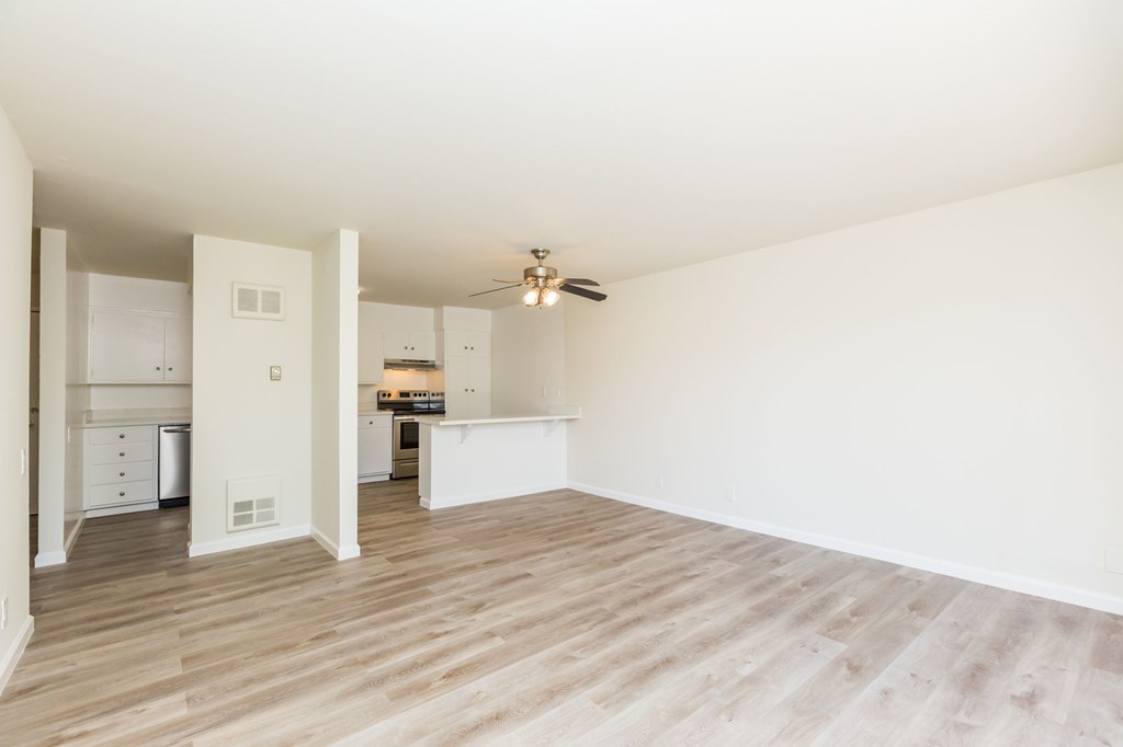 A room with a ceiling fan and a kitchen area in the background.