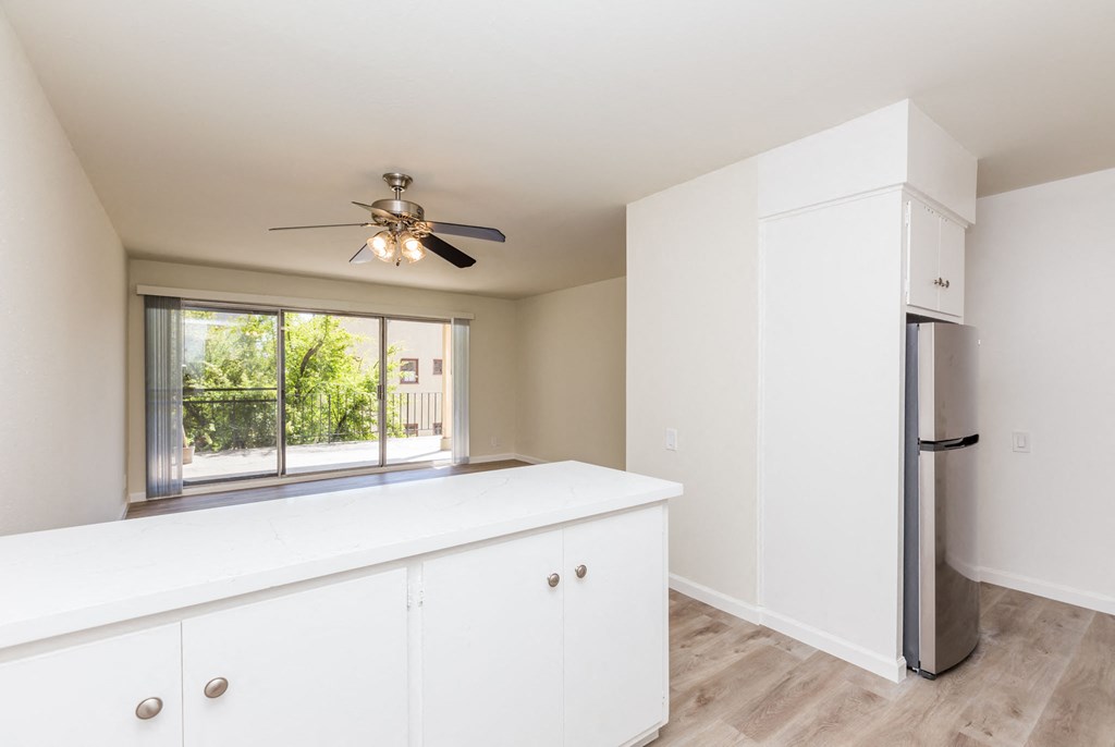 A white kitchen with a ceiling fan and a window.
