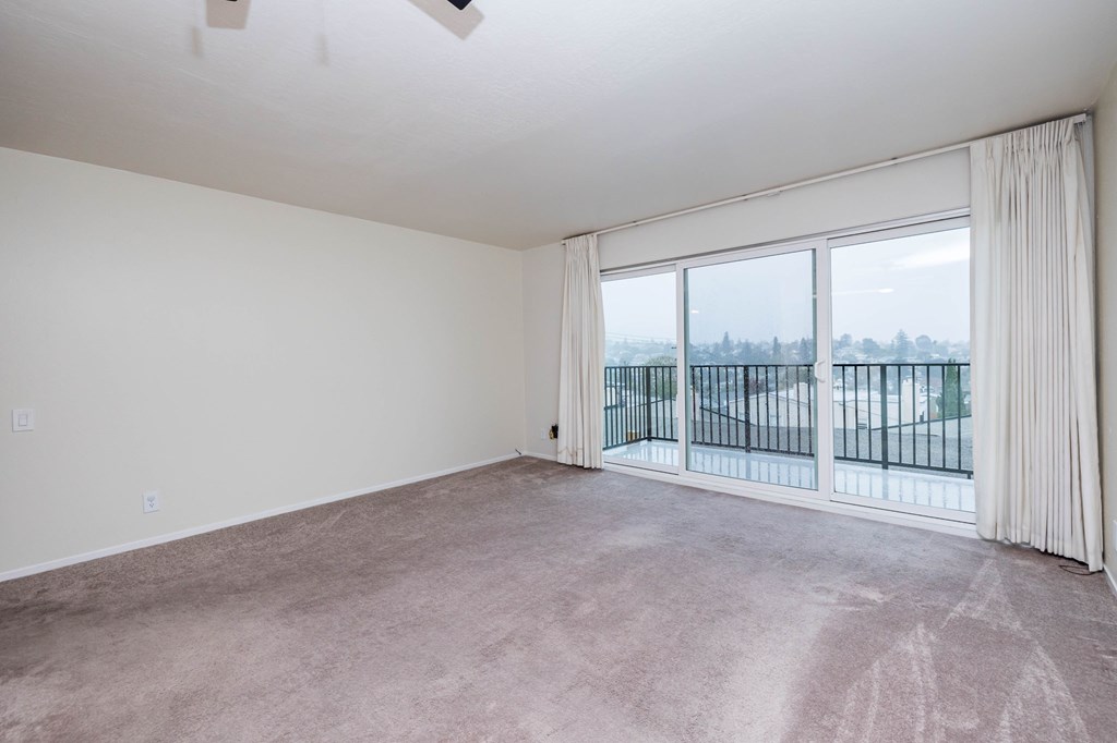 A room with a carpeted floor and a sliding glass door leading to a balcony.