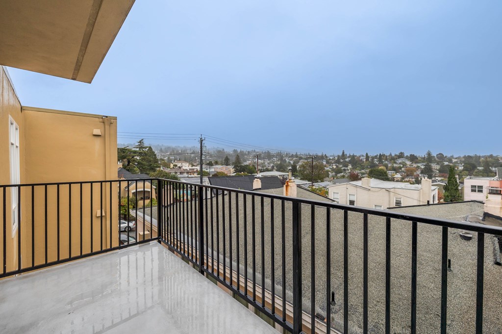 A balcony with a black railing overlooks a residential area.