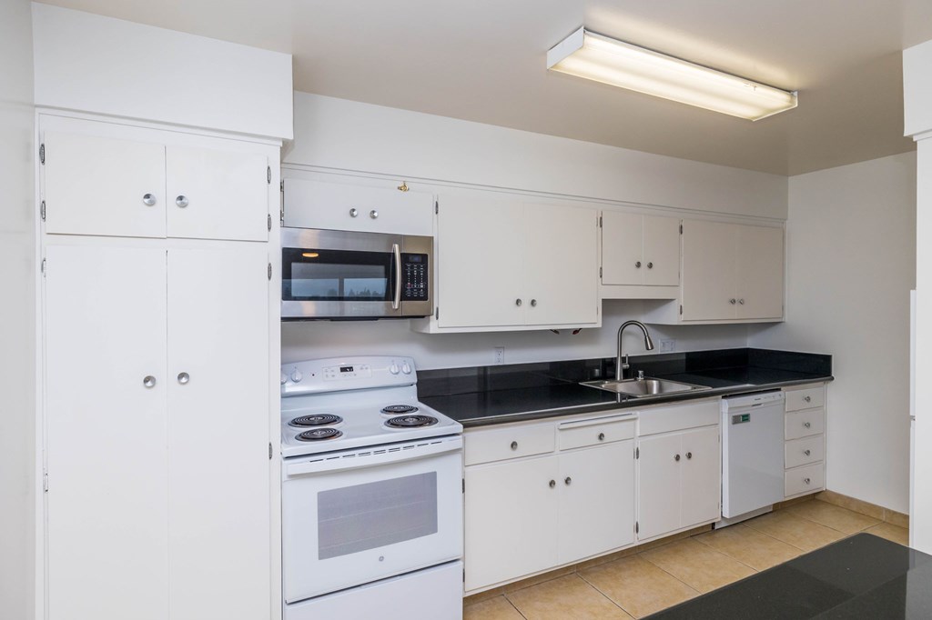 A white kitchen with a black countertop and a white stove.