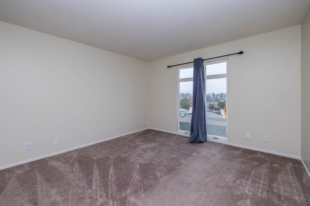 A room with a carpeted floor and a window with a blue curtain.