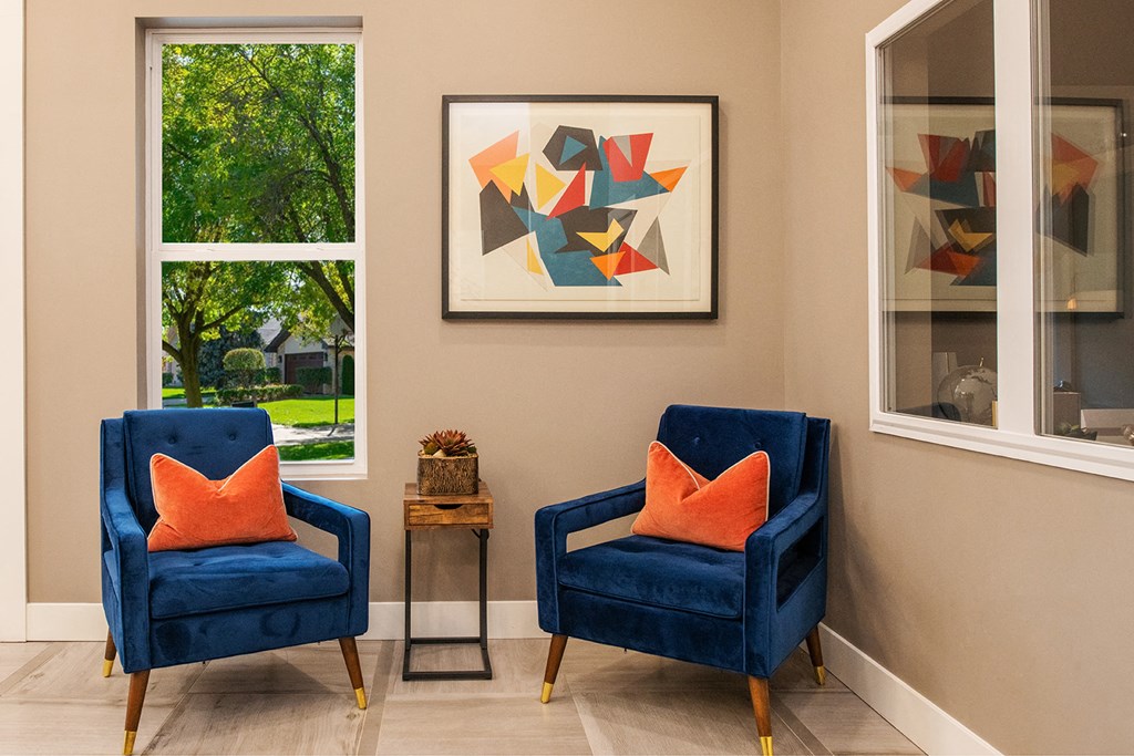 two blue chairs with orange pillows in a room with two windows