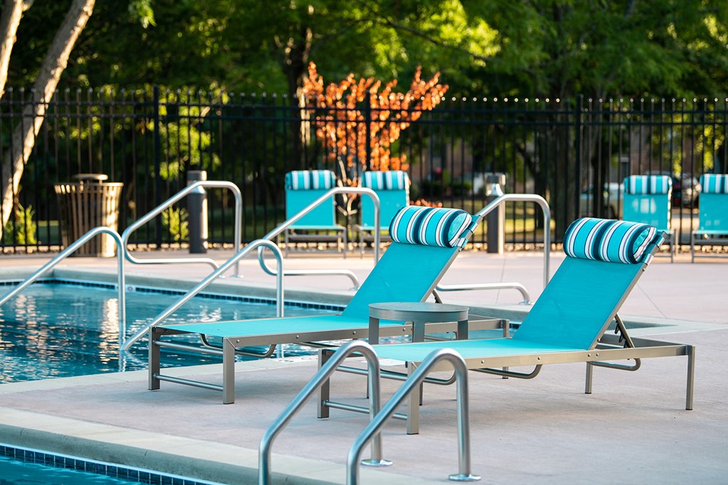 a pool with blue chaise lounge chairs and a poolside table