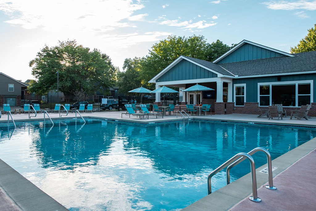 a swimming pool with lounge chairs and umbrellas in front of the clubhouse