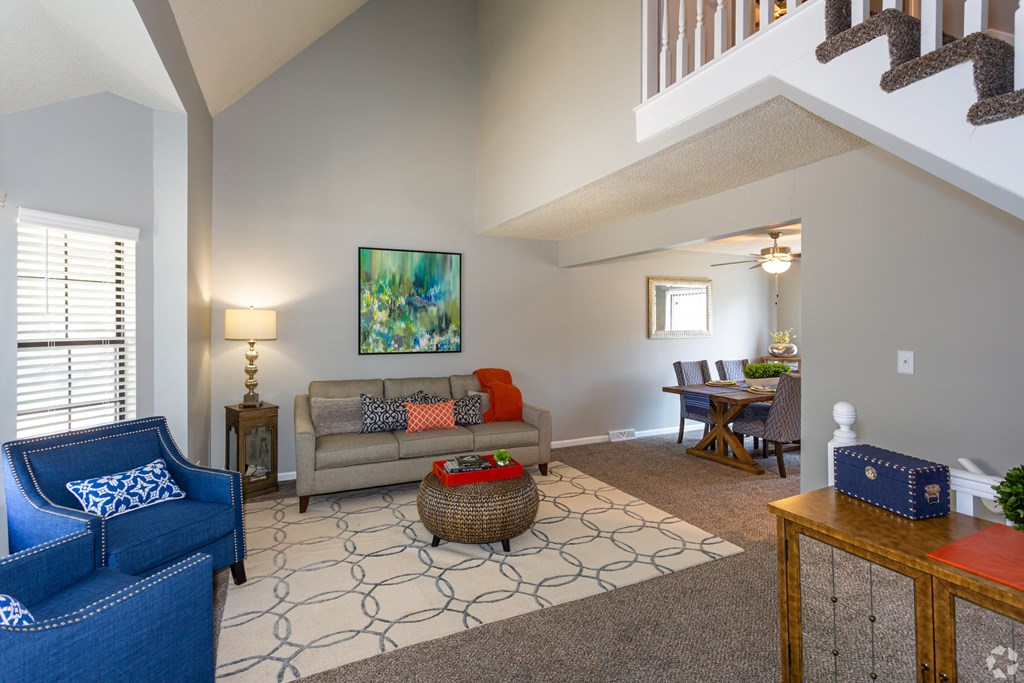 a living room with a staircase in the background and a dining room in the foreground