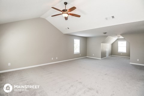 the spacious living room with ceiling fan and white carpet