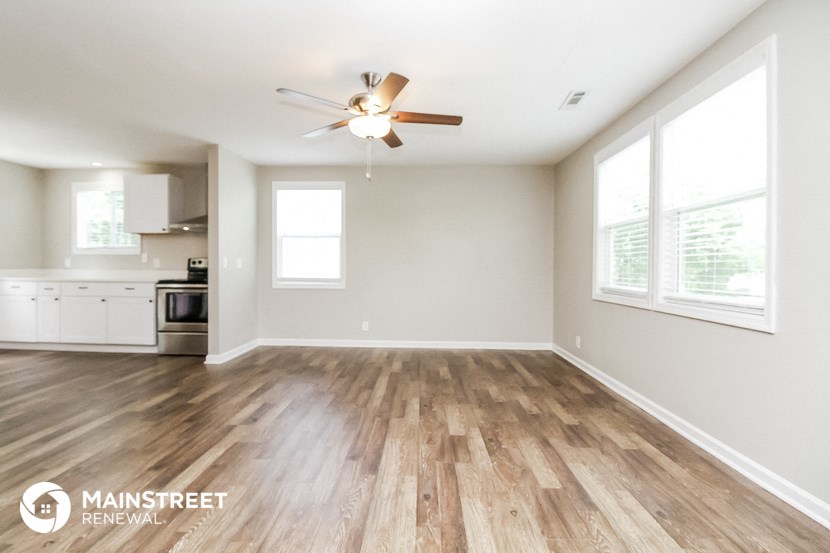 an empty living room with a ceiling fan and a kitchen