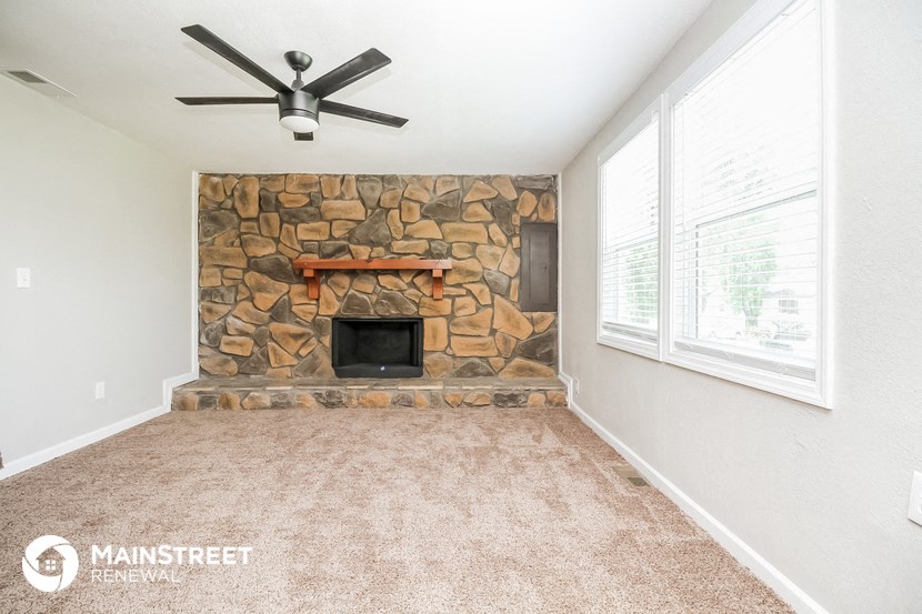 a living room with a stone fireplace and a ceiling fan