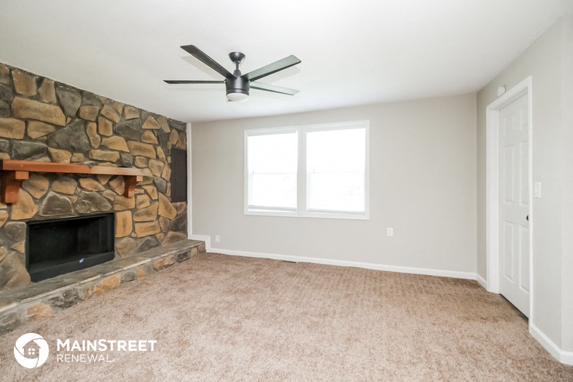 a living room with a stone fireplace and a ceiling fan