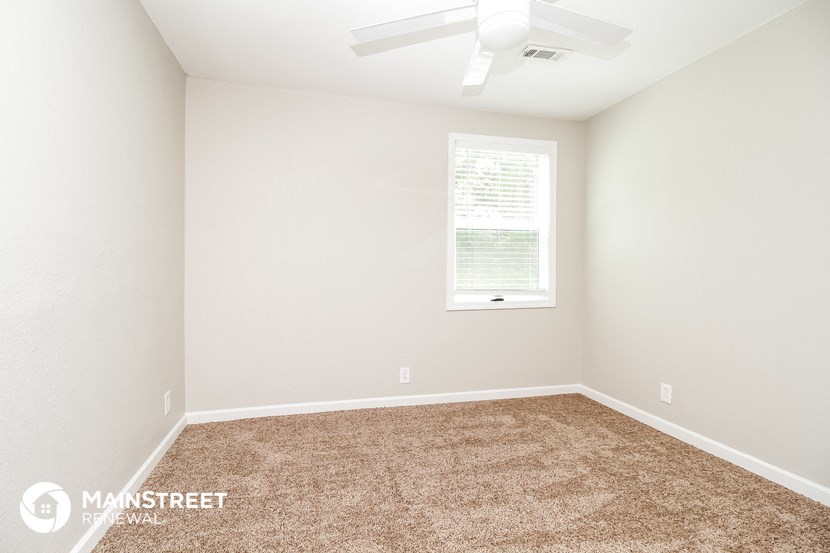the spacious bedroom with carpeted flooring and a ceiling fan