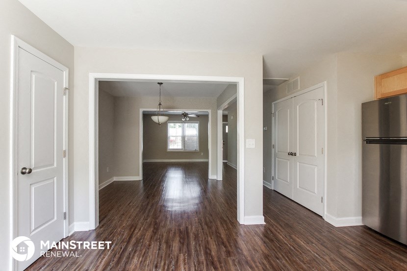 an empty living room and kitchen with wood floors and a refrigerator
